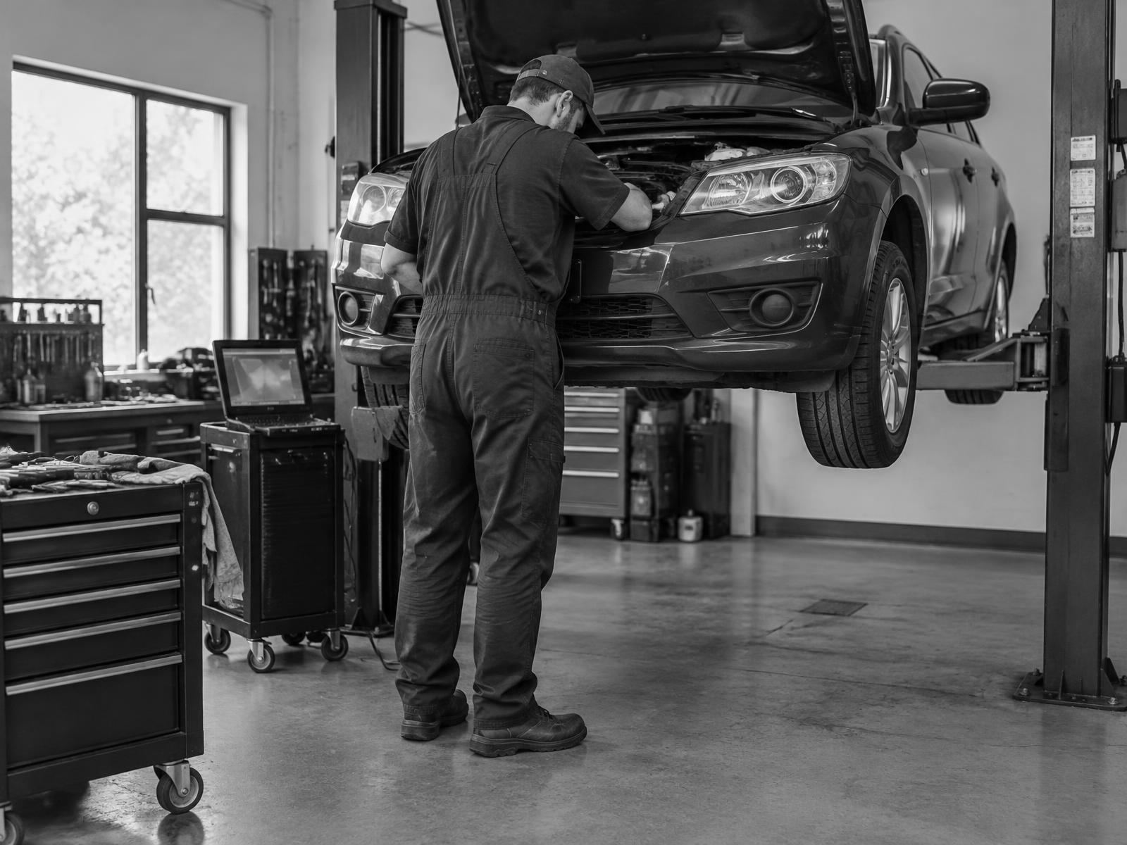 A technician working on a car raised on a hoist in an independent auto repair shop